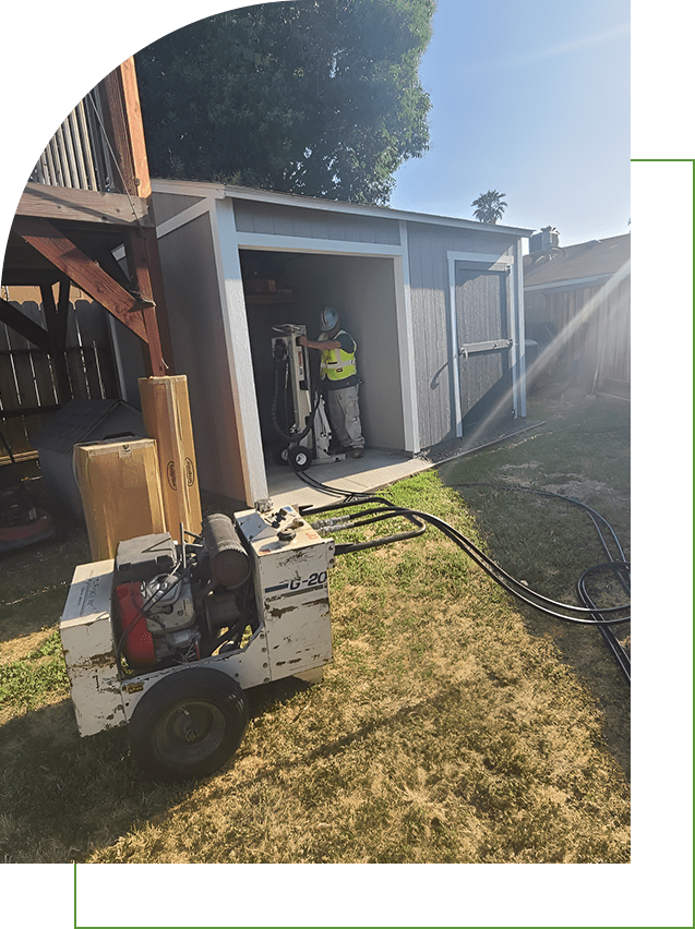 A worker uses a power machine outside a shed.