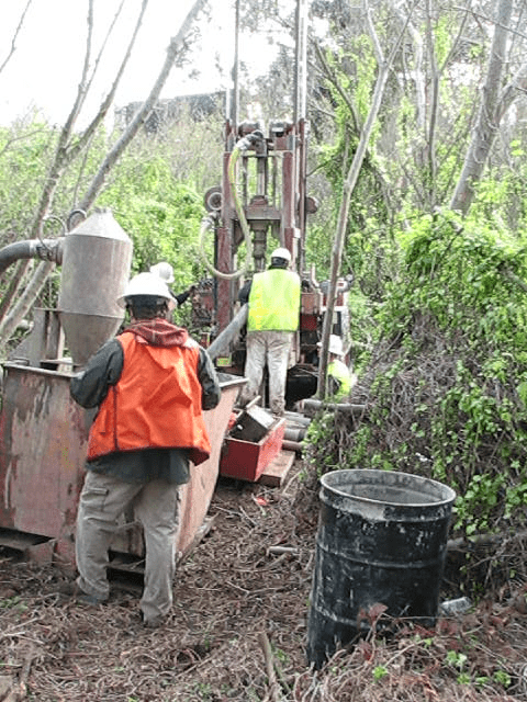 Workers operate drilling rig in forest.